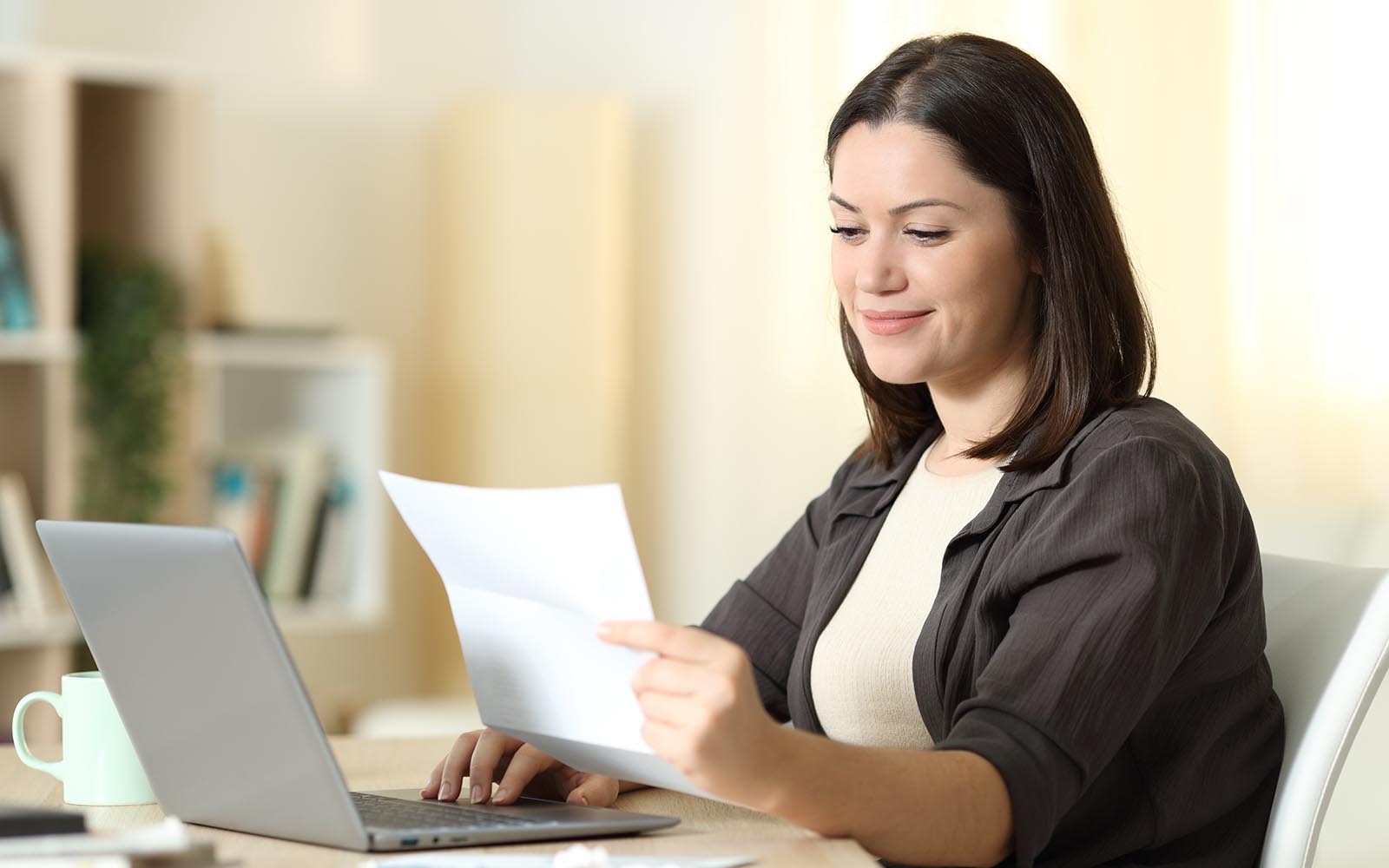 Woman reading a letter using laptop at home