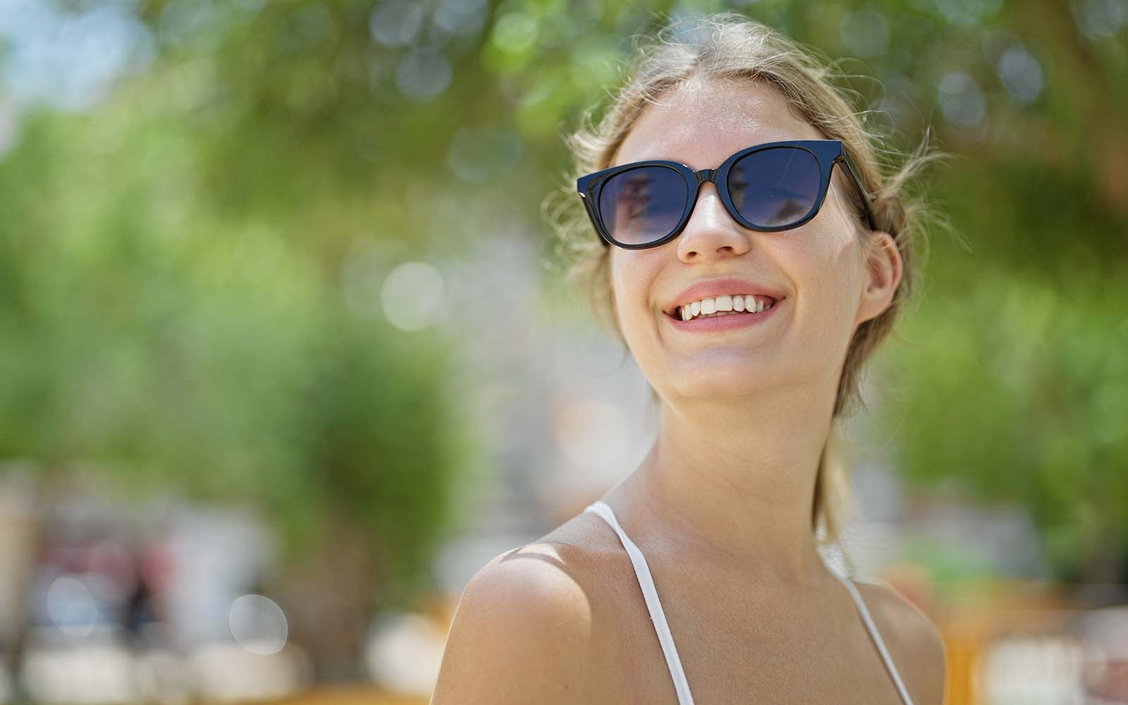 Young blonde woman wearing sunglasses looking to the sky smiling at park