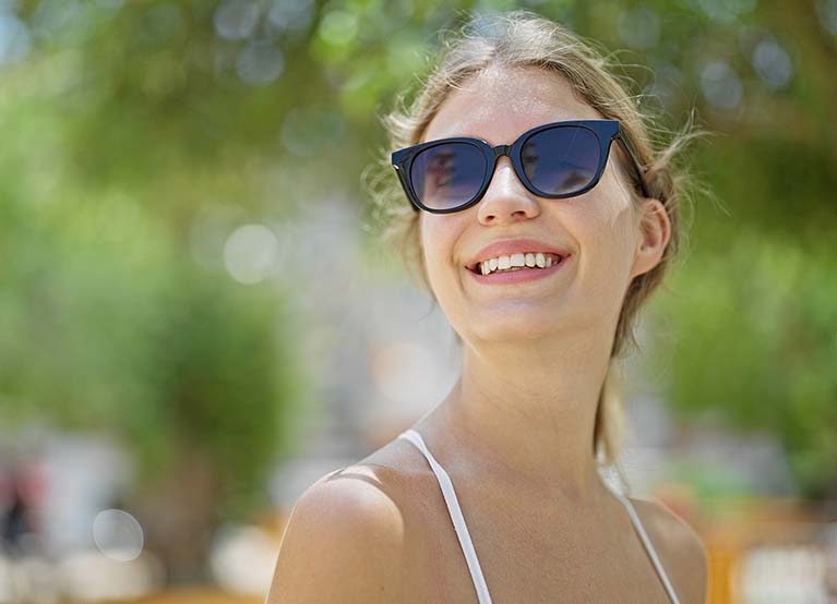 Young blonde woman wearing sunglasses looking to the sky smiling at park