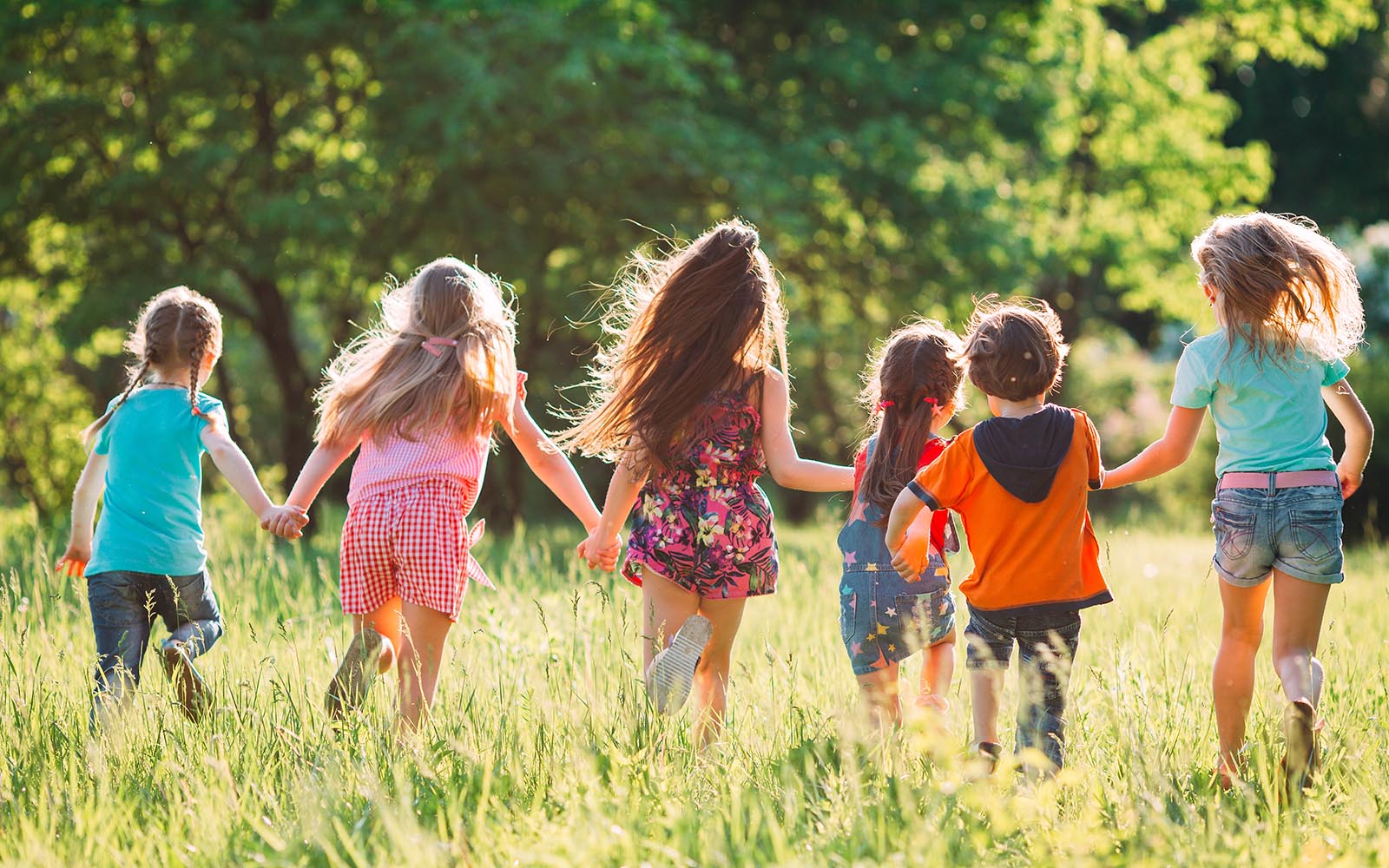 Large group of kids, friends boys and girls running in the park on sunny summer day in casual clothes .