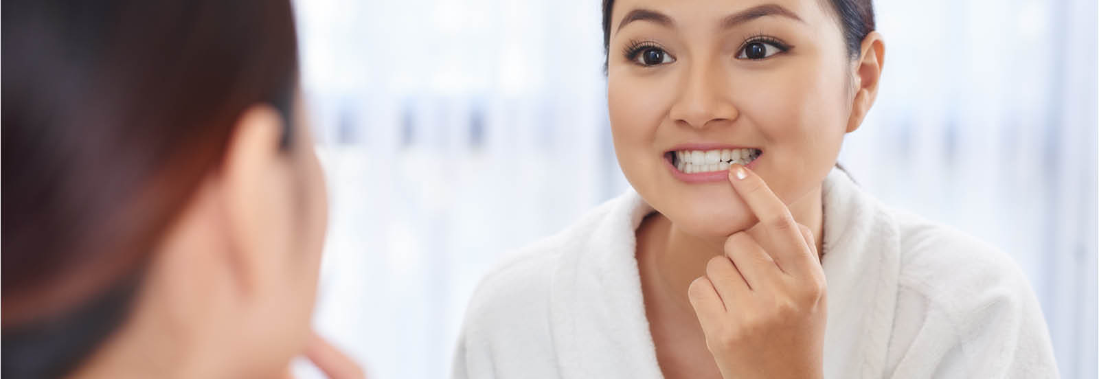 young woman looking at teeth and gums in the mirror 1600X552.jpg