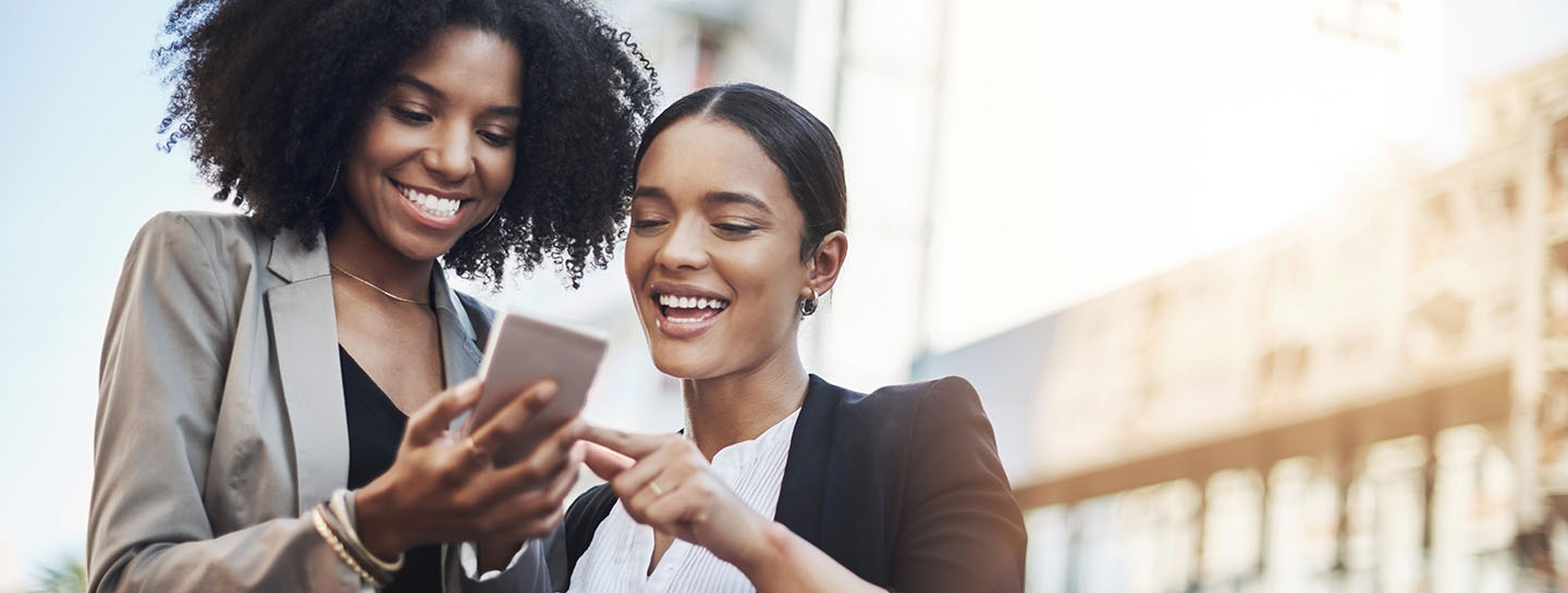 Reaching out to new networks. Shot of two businesswomen looking at something on a cellphone in the city.