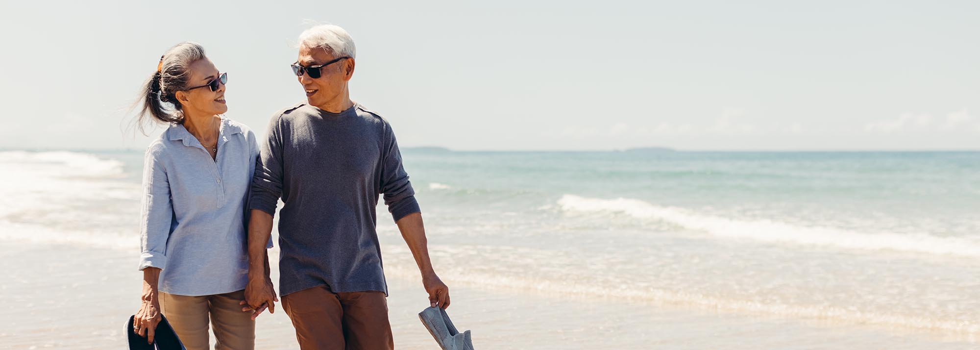Romantic Senior couple strolling happily along the beach in the sunshine and bright sky. Retirement concept and happy life.