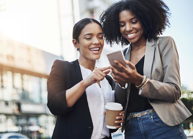 Reaching out to new networks. Shot of two businesswomen looking at something on a cellphone in the city.