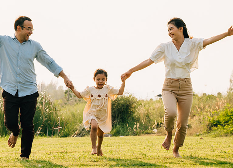 Asian family running and playing together in a beautiful nature setting, with a sunny sky and green grass all around, feeling carefree and happy, Happy Family Day Concept