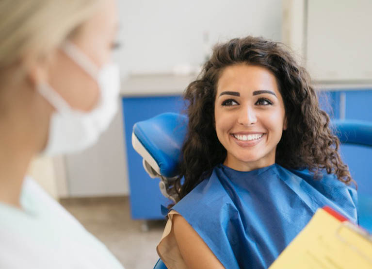 young woman with curly brown hair at the dentist smiling mobile 767x554.jpg