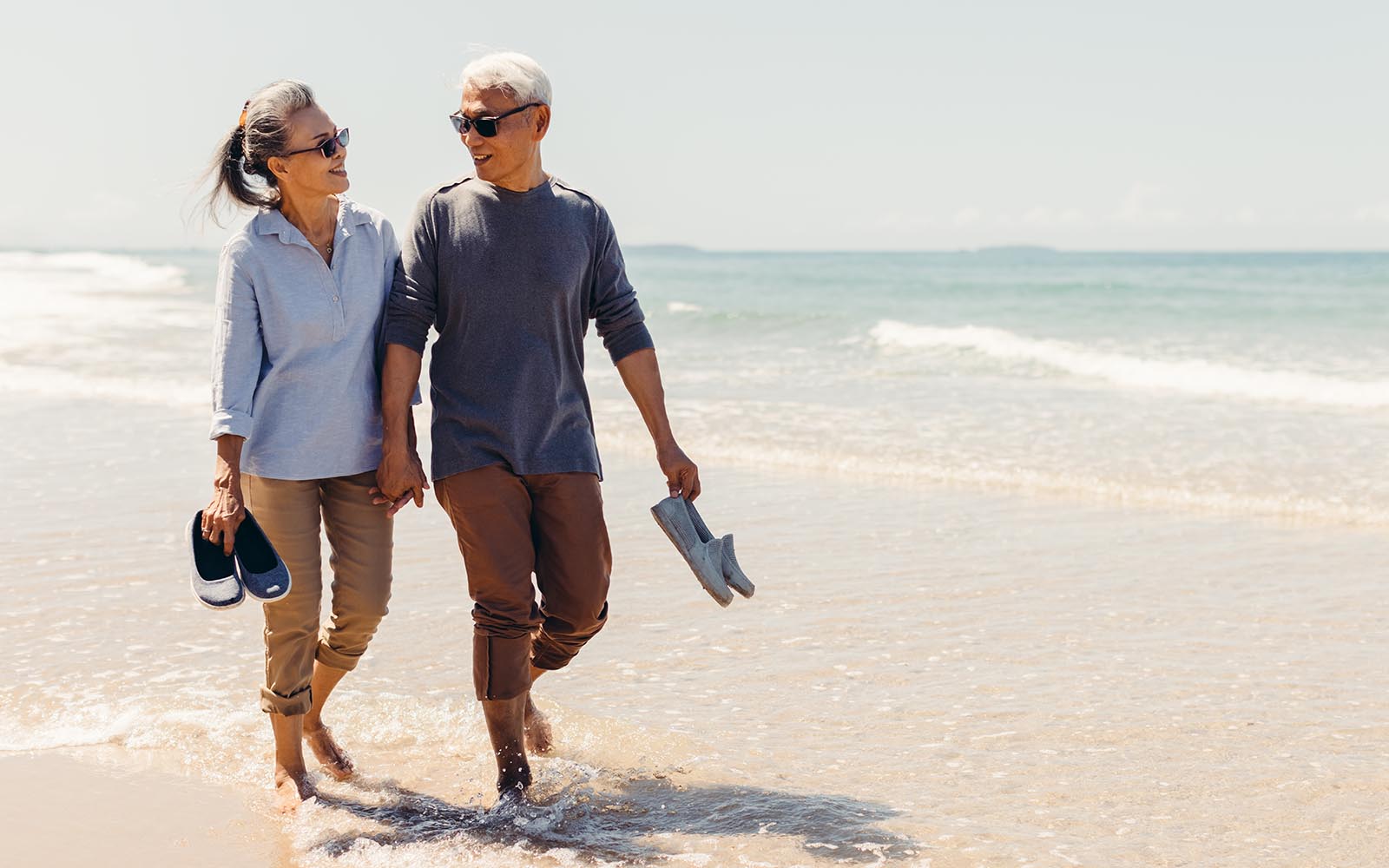 Romantic Senior couple strolling happily along the beach in the sunshine and bright sky. Retirement concept and happy life.