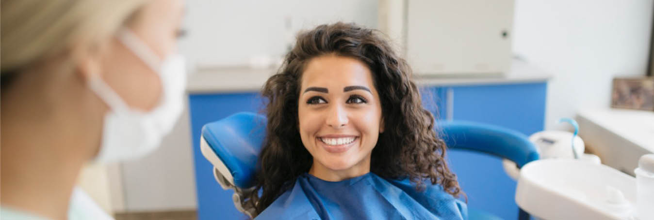 young woman with curly brown hair at the dentist smiling 1348X455.jpg